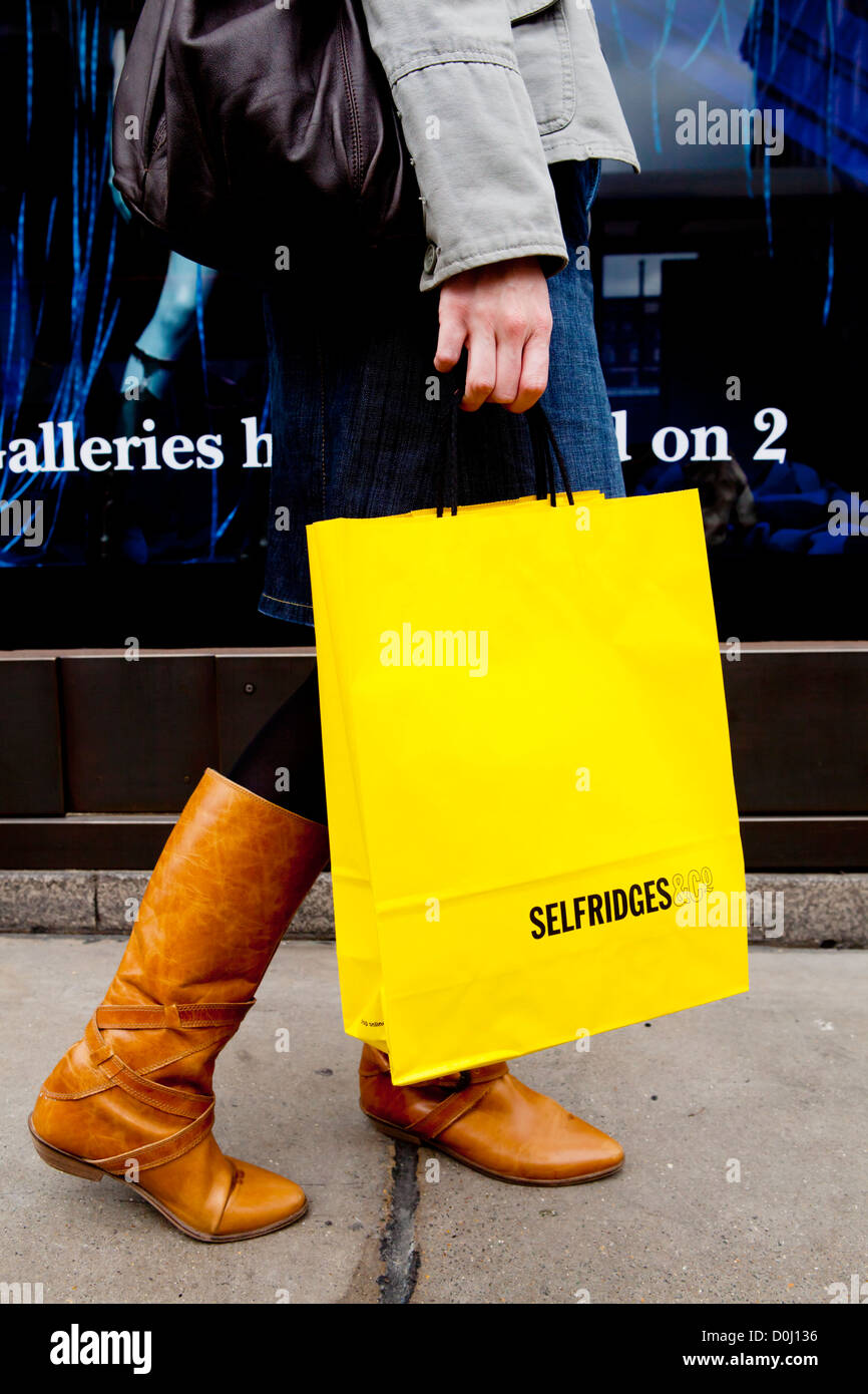 Eine junge Dame auf der Oxford Street mit hellen gelben Einkaufstaschen von Selfridges. Stockfoto