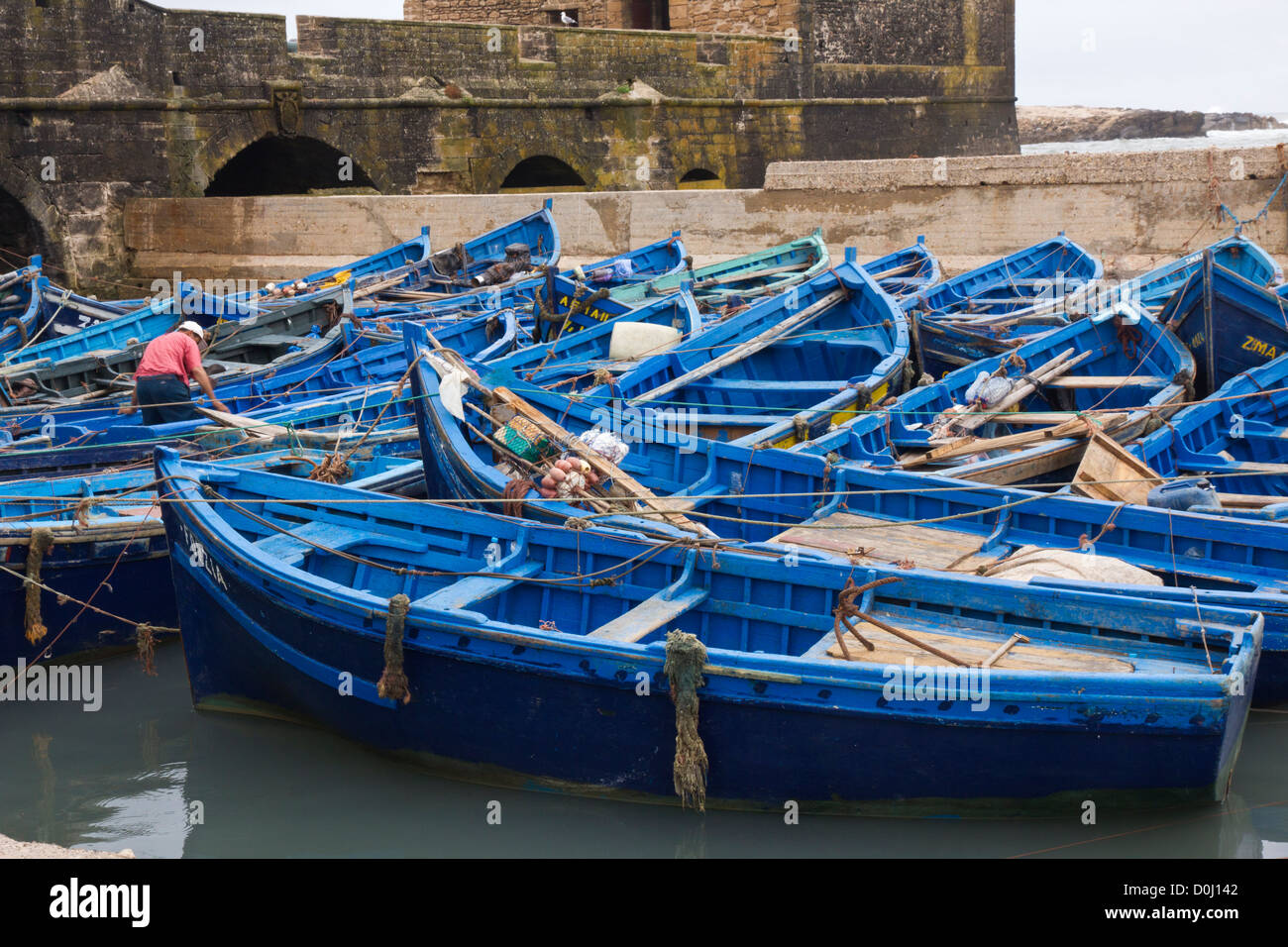 Mann arbeitet in der Masse der blauen Angelboote/Fischerboote im Hafen von Essaouira Stockfoto