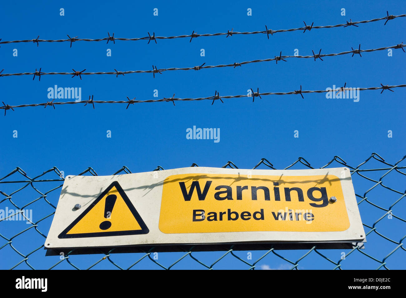 Warnschild am Stacheldraht gegen strahlend blauen Himmel. Stockfoto