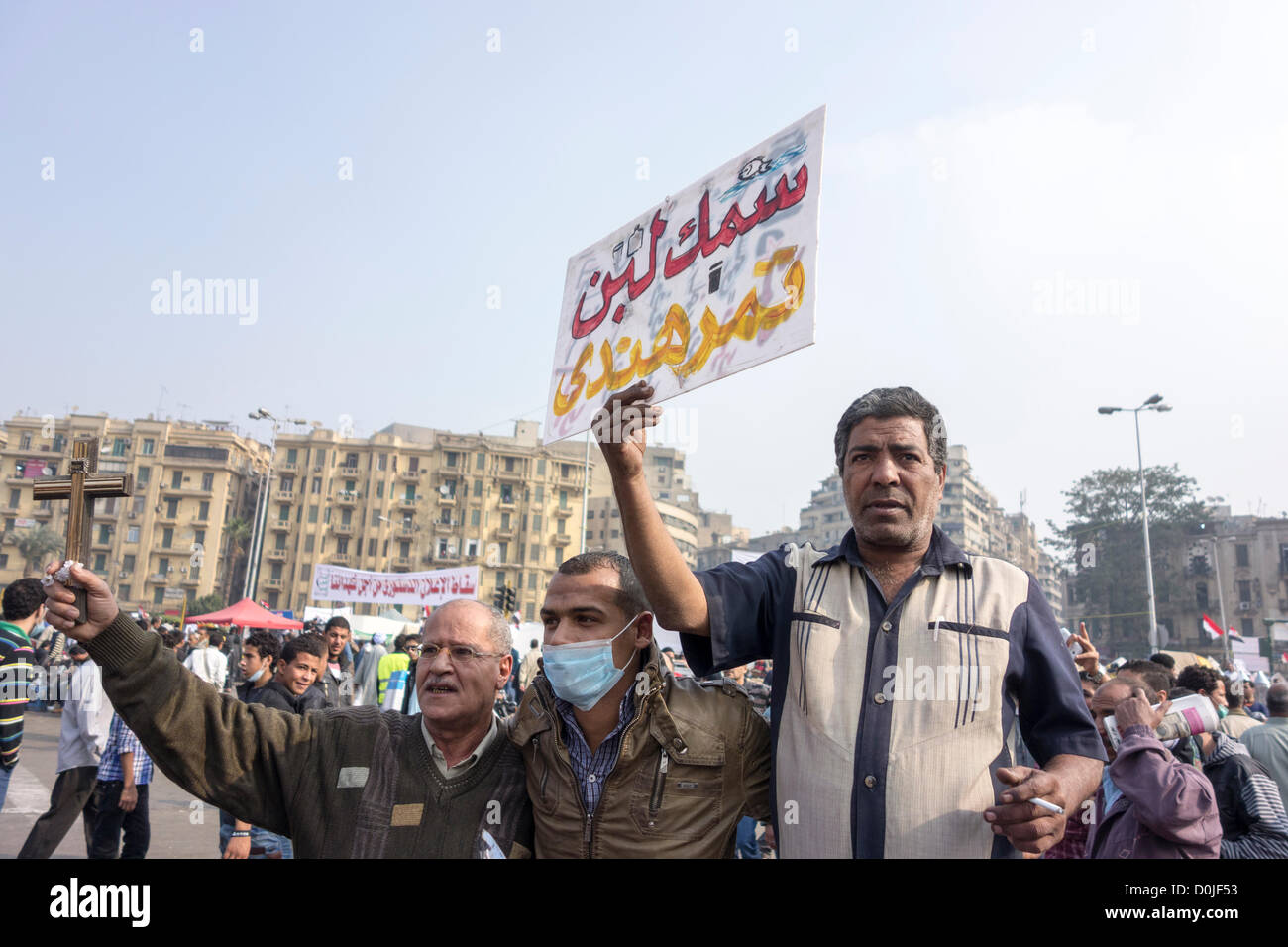 27. November 2012 Demonstranten protestieren gegen Präsident Morsi Annahme der absoluten Mächte auf dem Tahrir-Platz, Kairo, Ägypten hält man ein Schild in arabischer Sprache, das bedeutet "Dinge sind ein totales Durcheinander;" Eine andere hält ein Kreuz in Solidarität. Stockfoto