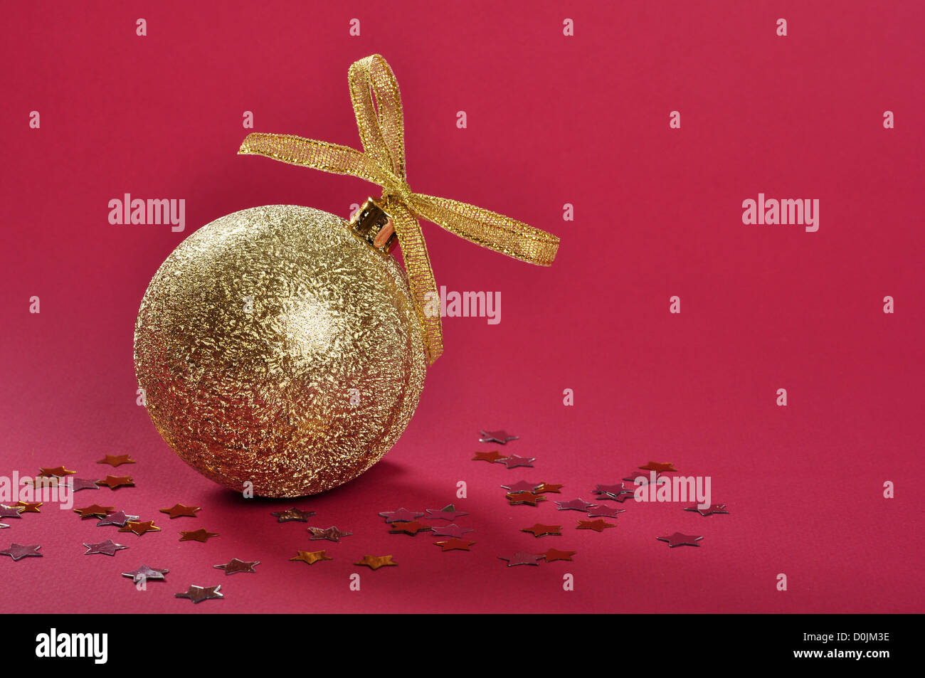 Goldglitter Weihnachtskugel mit Schleife und Bogen über rotem Grund. Stockfoto