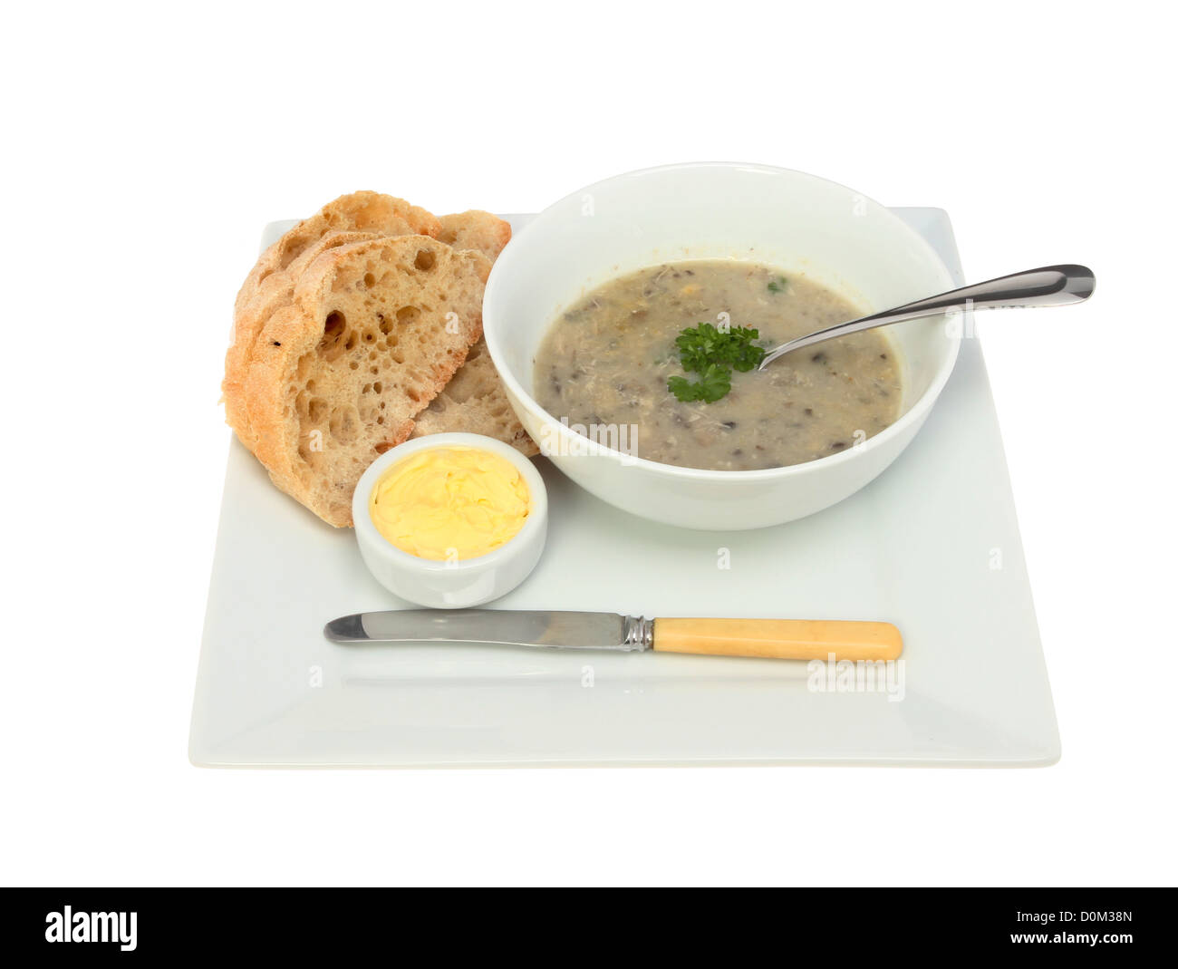 Suppe mit Brot und Butter, Messer und Löffel auf einem Teller isoliert gegen weiß Stockfoto