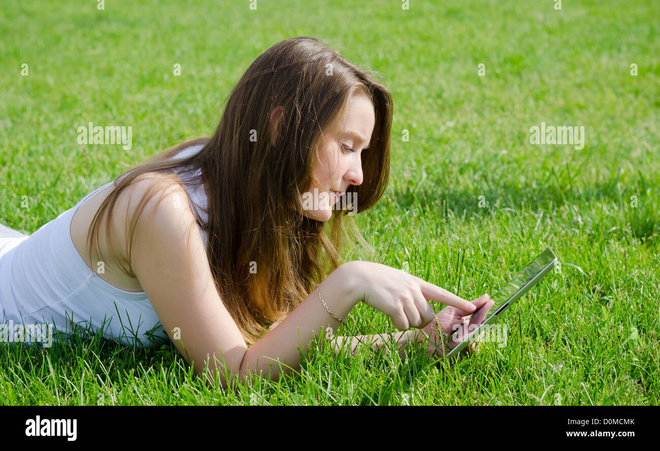 Junge Dame oder Studentin liegend auf dem Bauch in dem grünen Rasen mit einem Tablet-notebook Stockfoto