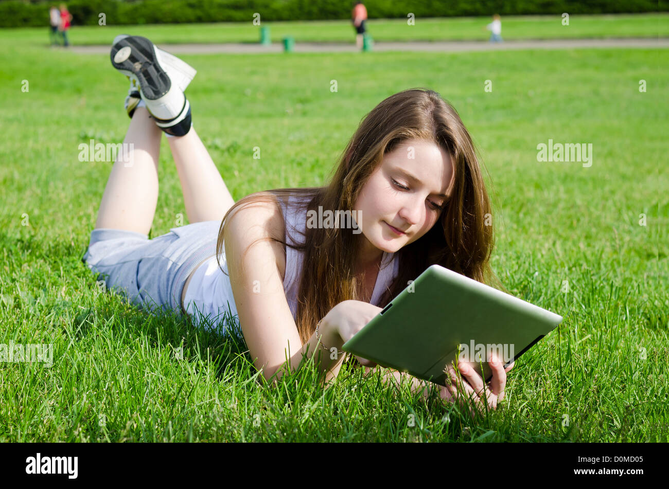 Junge Dame oder Studentin liegend auf dem Bauch in dem grünen Rasen mit einem Tablet-notebook Stockfoto