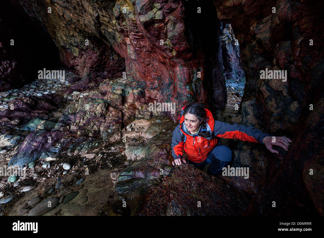 Frau Klettern auf Felsen innen Meereshöhle am Plemont, Jersey, Kanalinseln, Großbritannien Stockfoto