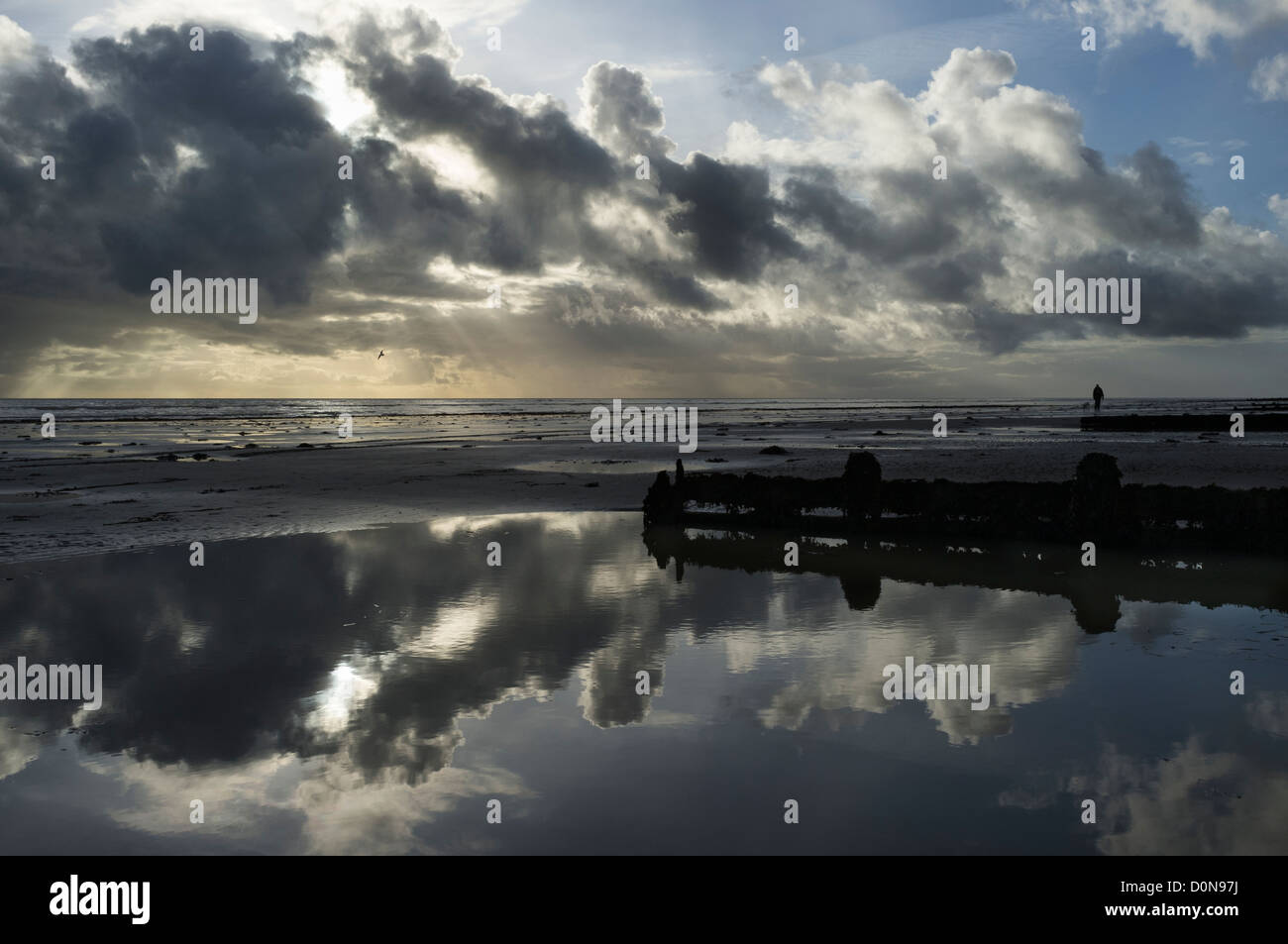 Wolken spiegeln sich in einem Pool links von der zurückweichenden Flut an einem nassen Strand Stockfoto