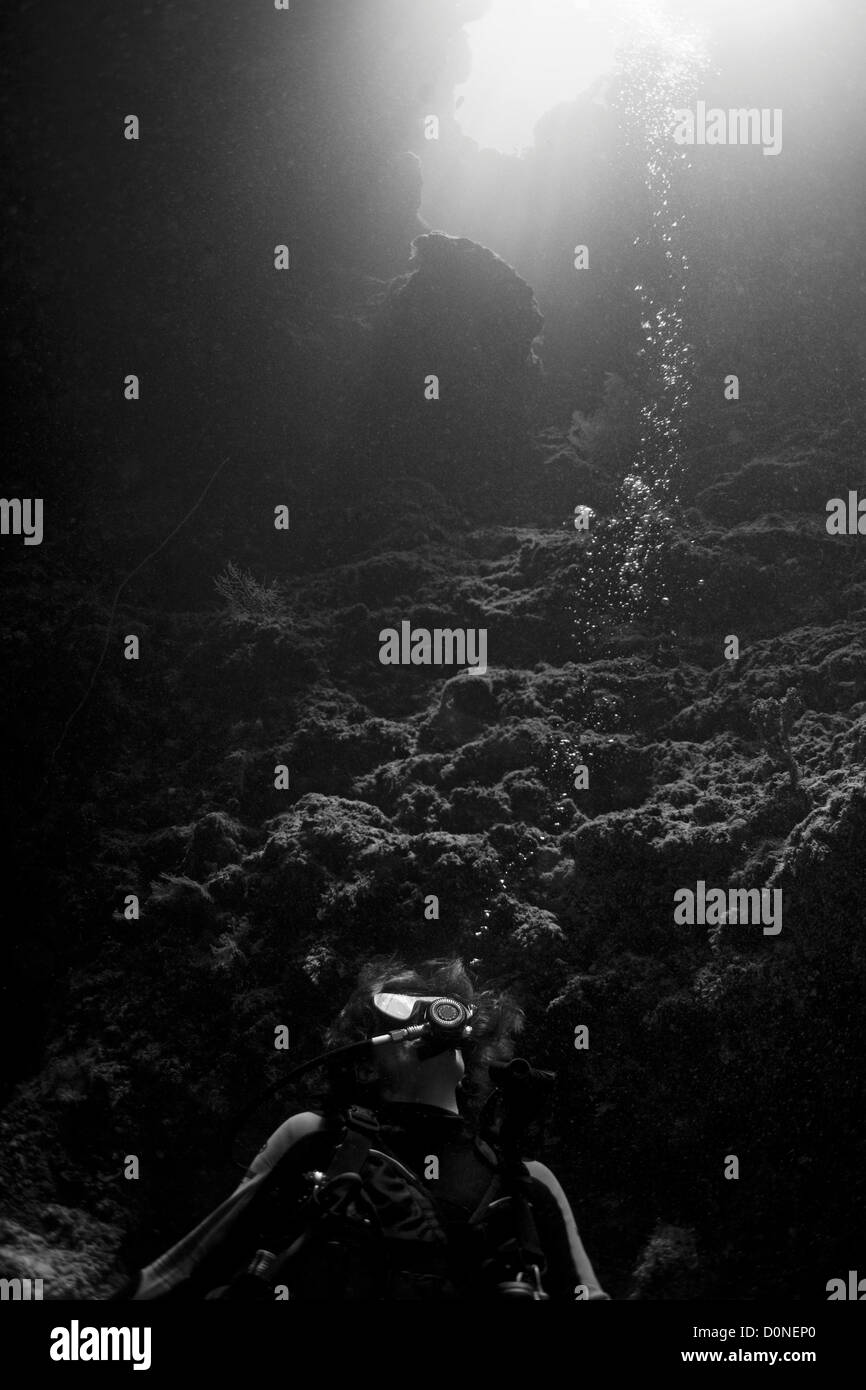 Ein Taucher schaut zu Sonnenlicht streaming durch den Eingang zu einer Unterwasser-Höhle, Sipadan, Sabah, Malaysia. Stockfoto