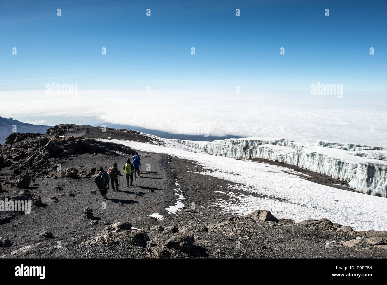 KILIMANDSCHARO, Tansania – Eine Gruppe von Kletterern beginnt den Abstieg vom Gipfel des Kilimandscharo, mit permanenten Gletschern, die rechts zu sehen sind. Der Kilimandscharo ist mit 19.341 Metern der höchste Gipfel Afrikas und einer der bekanntesten freistehenden Berge der Welt. Der Berg hat drei vulkanische Kegel und liegt im Norden Tansanias nahe der Grenze zu Kenia. Trotz seiner Nähe zum Äquator unterstützt die hohe Erhebung des Kilimandscharo permanente Eisfelder und Gletscher an seinen oberen Hängen. Der Berg zieht jährlich Tausende von Kletterern an, die versuchen, Uh zu erreichen Stockfoto