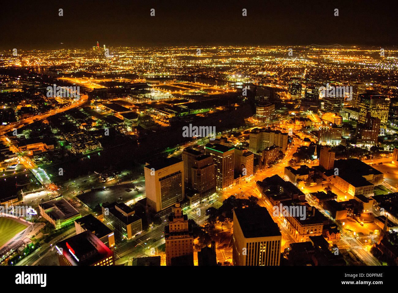 NEWARK, New Jersey, Vereinigte Staaten – ein Blick aus der Vogelperspektive auf die Innenstadt von Newark bei Nacht, aufgenommen von einem Hubschrauber in einer Höhe von etwa 500 Metern, zeigt die lebhafte Stadtlandschaft der Stadt. Die hellen Lichter der Straßen, Gebäude und Wahrzeichen bilden einen glitzernden Wandteppich vor der dunklen Kulisse und bieten einen beeindruckenden Blick auf die größte Stadt New Jerseys. Hinweis: Aufgrund der schwierigen Lichtverhältnisse bei Nachtaufnahmen ist ein gewisses ISO-Rauschen bei voller Auflösung sichtbar. Stockfoto