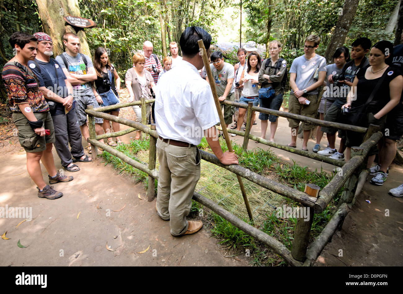 Cu Chi Tunnel Punji Trap Demonstration Ho Chi Minh Stadt Vietnam // HO CHI MINH STADT, Vietnam - Ein Reiseleiter zeigt eine erhaltene Punji Falle an der historischen Stätte der Cu Chi Tunnel und zeigt Besuchern eine der Verteidigungsmaßnahmen während des Vietnamkriegs. Die getarnte Falle verfügt über eine verborgene Grube mit Metallspitzen, die die Art der Verteidigungstechnik repräsentieren, die üblicherweise während des Konflikts angewendet wird. Die Cu-Chi-Tunnel nordwestlich von Ho-Chi-Minh-Stadt dienten als ausgedehntes unterirdisches Netzwerk, das von vietnamesischen Truppen genutzt wurde. Die Demonstration ist Teil der Bildungsveranstaltung des Standorts Stockfoto Cu Chi Tunnel Punji Trap Demonstration Ho Chi Minh Stadt Vietnam // HO CHI MINH STADT, Vietnam - Ein Reiseleiter zeigt eine erhaltene Punji Falle an der historischen Stätte der Cu Chi Tunnel und zeigt Besuchern eine der Verteidigungsmaßnahmen während des Vietnamkriegs. Die getarnte Falle verfügt über eine verborgene Grube mit Metallspitzen, die die Art der Verteidigungstechnik repräsentieren, die üblicherweise während des Konflikts angewendet wird. Die Cu-Chi-Tunnel nordwestlich von Ho-Chi-Minh-Stadt dienten als ausgedehntes unterirdisches Netzwerk, das von vietnamesischen Truppen genutzt wurde. Die Demonstration ist Teil der Bildungsveranstaltung des Standorts Stockfoto