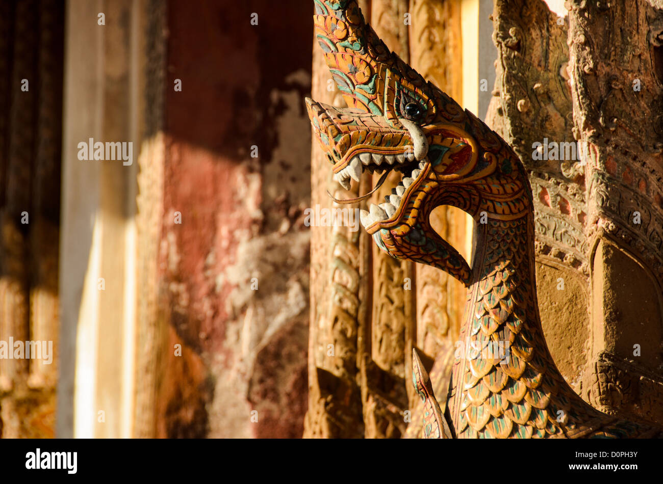 Wat Sisaket Naga Serpent Vientiane Laos // VIENTIANE, Laos — Eine geschnitzte hölzerne Nāga Schlangengottheit ist Teil der Außenwand des Wat Sisaket in Vientiane. Der Tempel wurde 1818 während der Regierungszeit von König Anouvong erbaut und repräsentiert eher den siamesischen Architekturstil als das traditionelle laotische Design. Der Wat Sisaket gilt weithin als der älteste noch existierende Tempel in Vientiane, nachdem er die siamesische Invasion von 1828 überlebt hat, die einen Großteil der Stadt zerstörte. Der Tempel ist berühmt für seine tausenden Buddha-Bilder, die in Nischen entlang der Innenwände untergebracht sind. Nāga Schlangengottheiten haben in Bud eine bedeutende Bedeutung Stockfoto