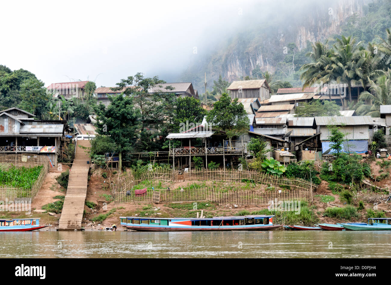 Nong Khiaw Dorf Uferpromenade Luang Prabang Laos // NONG KHIAW, Laos — Häuser säumen die Uferpromenade im Dorf Nong Khiaw im Norden Laos. Die Siedlung liegt am Fluss Nam Ou in der Provinz Luang Prabang, zwischen dramatischen Kalksteinkarstbergen. Nong Khiaw dient als Tor zum ländlichen Norden von Laos und wird häufig als Basis für die Erkundung des umliegenden bergigen Geländes genutzt. Das Dorf hat sich als Haltepunkt entlang der Nam ou River Route entwickelt, die Luang Prabang mit der chinesischen Grenze verbindet. Das Gebiet ist Teil der größeren nördlichen Region Laos, die für ihr traditionelles La bekannt ist Stockfoto