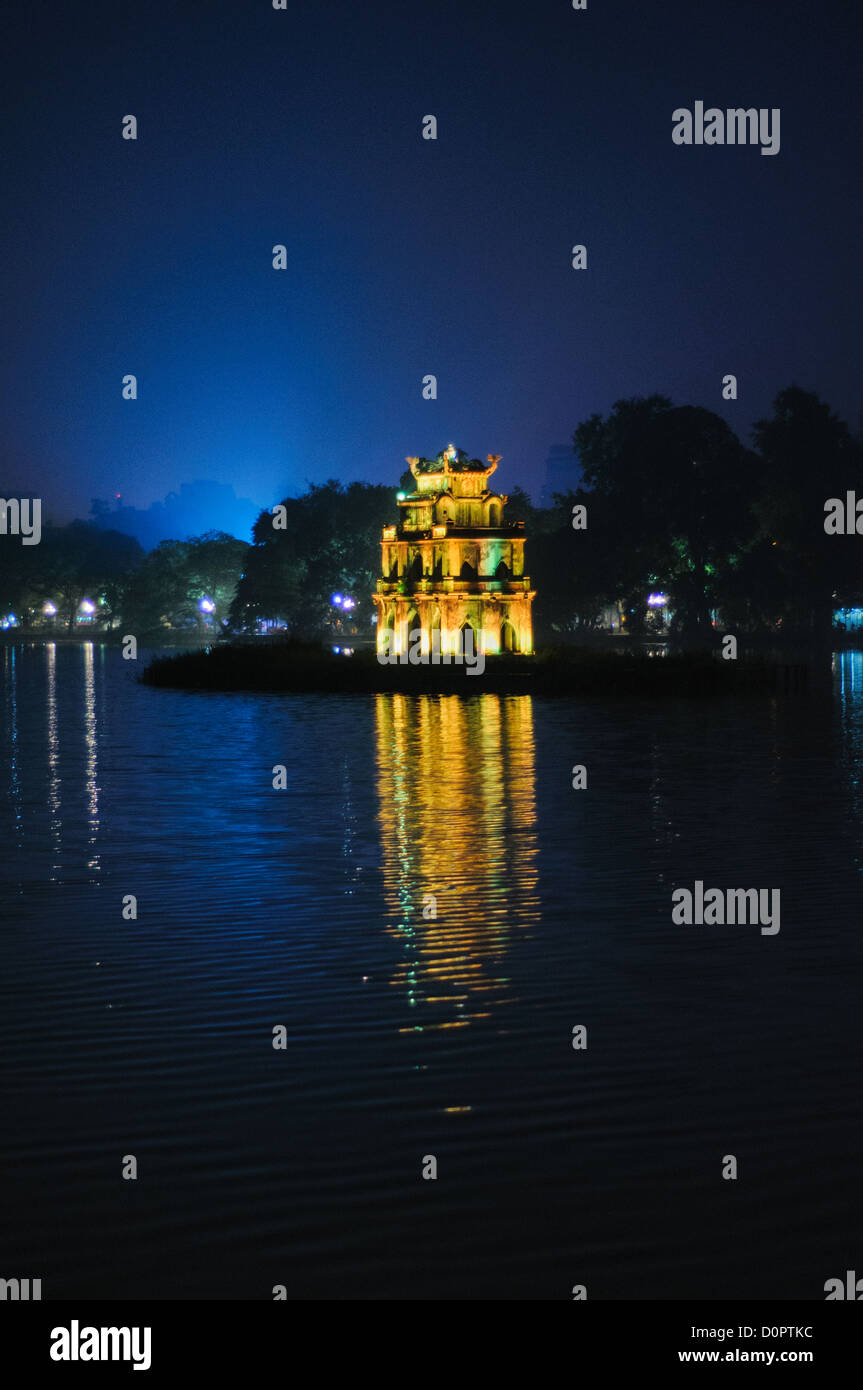 Turtle Tower Hoan Kiem Lake Hanoi Vietnam // HANOI, Vietnam — Turtle Tower (Thap Rua), beleuchtet bei Nacht, steht auf einer kleinen Insel im Hoan Kiem Lake im Zentrum von Hanoi. Das historische Denkmal, das 1886 während der französischen Kolonialzeit erbaut wurde, erinnert an die legendäre Geschichte der goldenen Schildkröte des Sees. Die Lichter der umliegenden Gebäude spiegeln sich unter einem tiefblauen Abendhimmel auf der Oberfläche des Sees. Stockfoto