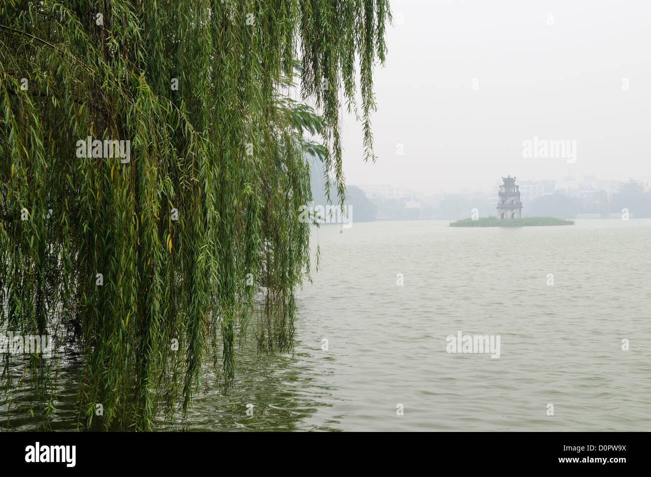 HANOI, Vietnam - Schildkröte Turm (Thap Rua), auf einer kleinen Insel in der Mitte der Hoan Kiem See im Herzen von Hanoi ist teilweise verdeckt von einer dicken Morgens Nebel. Im Vordergrund auf der linken Seite, sind einige der niedrig hängenden Bäume am Ufer des Sees. Stockfoto