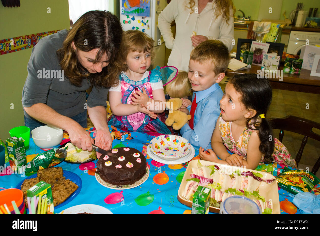 Kinder bei einer Geburtstag-Partei-Mama schneidet sich die Geburtstagstorte Stockfoto