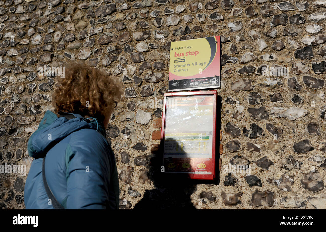 Frau Überprüfung Busfahrplan auf alten Feuerstein Wand im ländlichen Dorf Einstellung Stockfoto