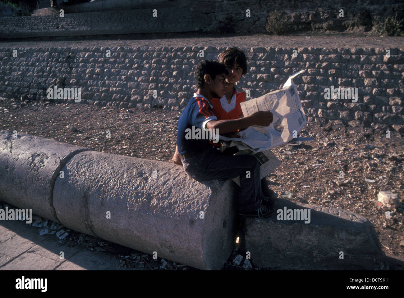 Zwei junge Jungen lasen 1982 eine Zeitung über eine gefallene römische Kolonne in Amman Stockfoto