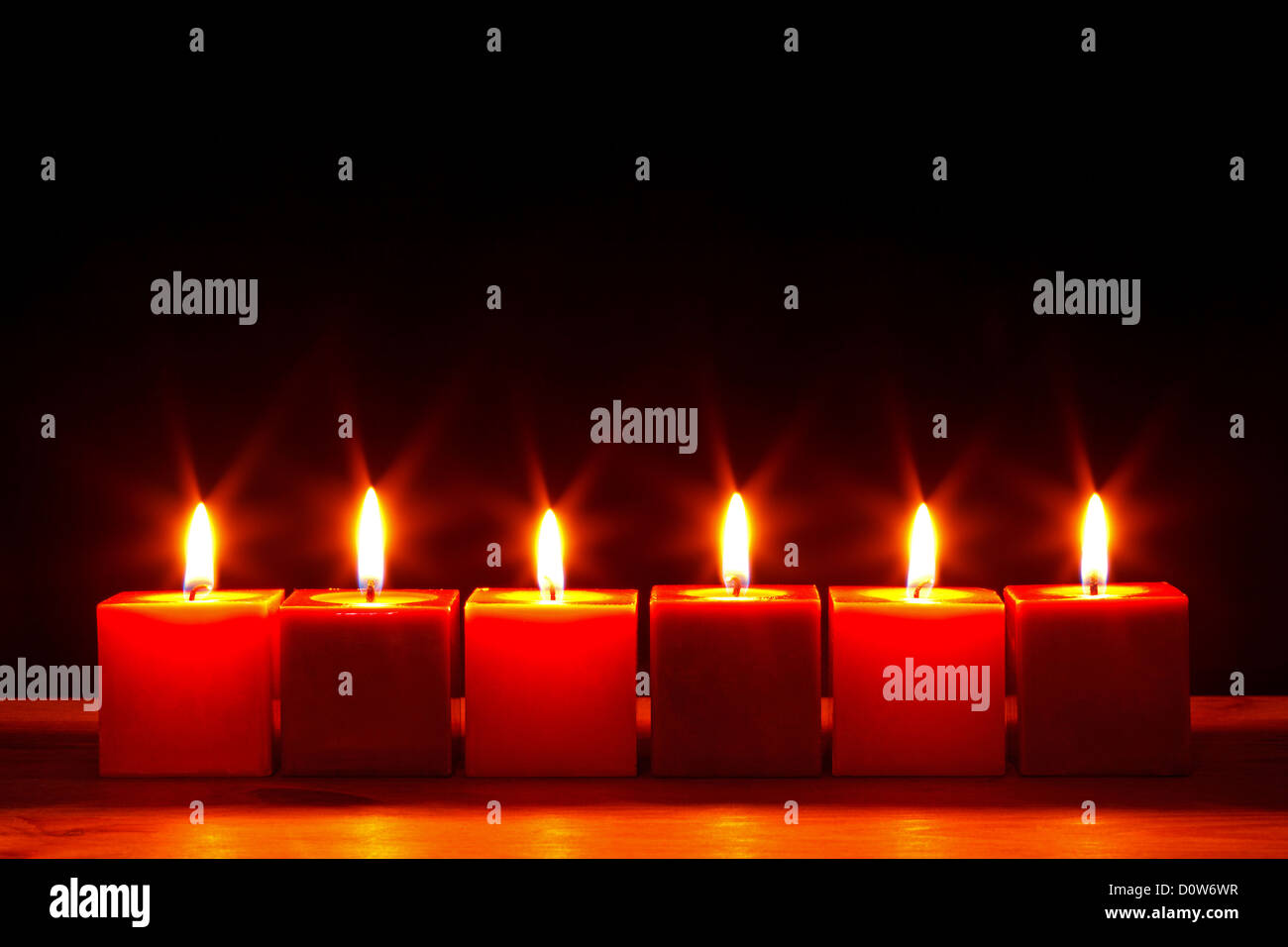 Still-Leben Foto von sechs quadratischen roten Kerzen brennen hell vor einem schwarzen Hintergrund. Stockfoto