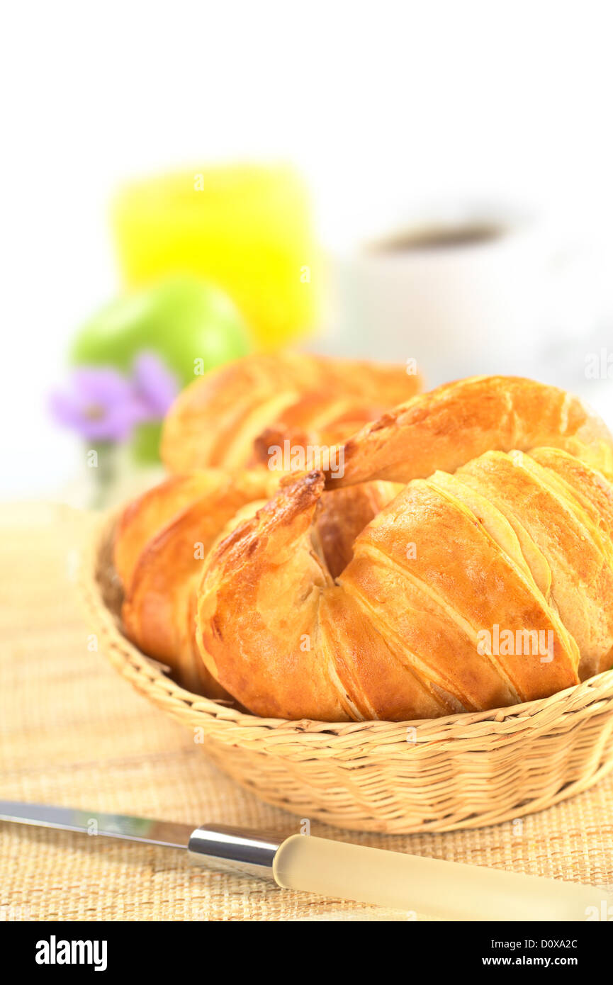 Frische Croissants im Brotkorb mit Kaffee, Orangensaft und ein grüner Apfel auf der Rückseite Stockfoto