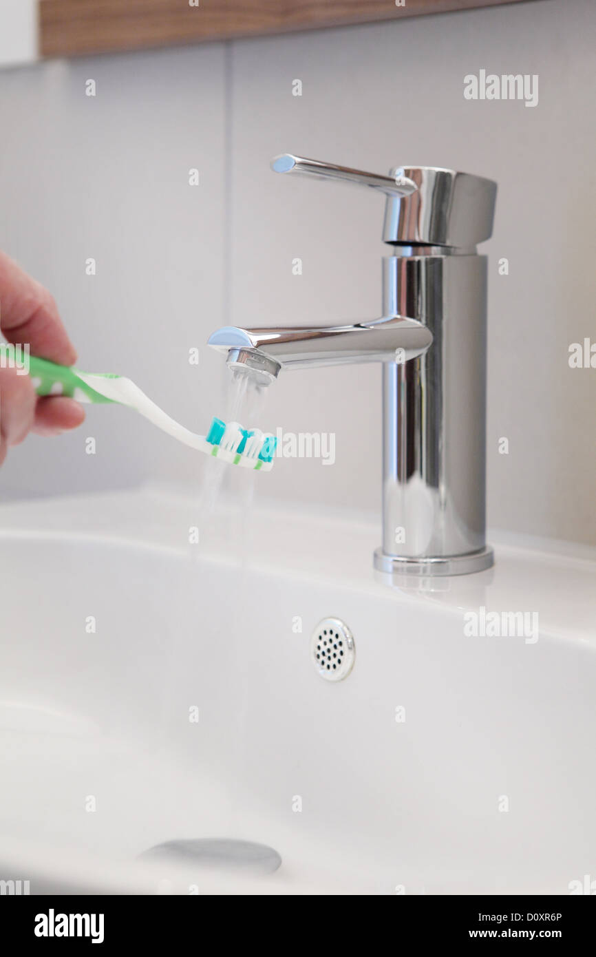 Fließendes Wasser auf Zahnbürste in Waschbecken Stockfoto