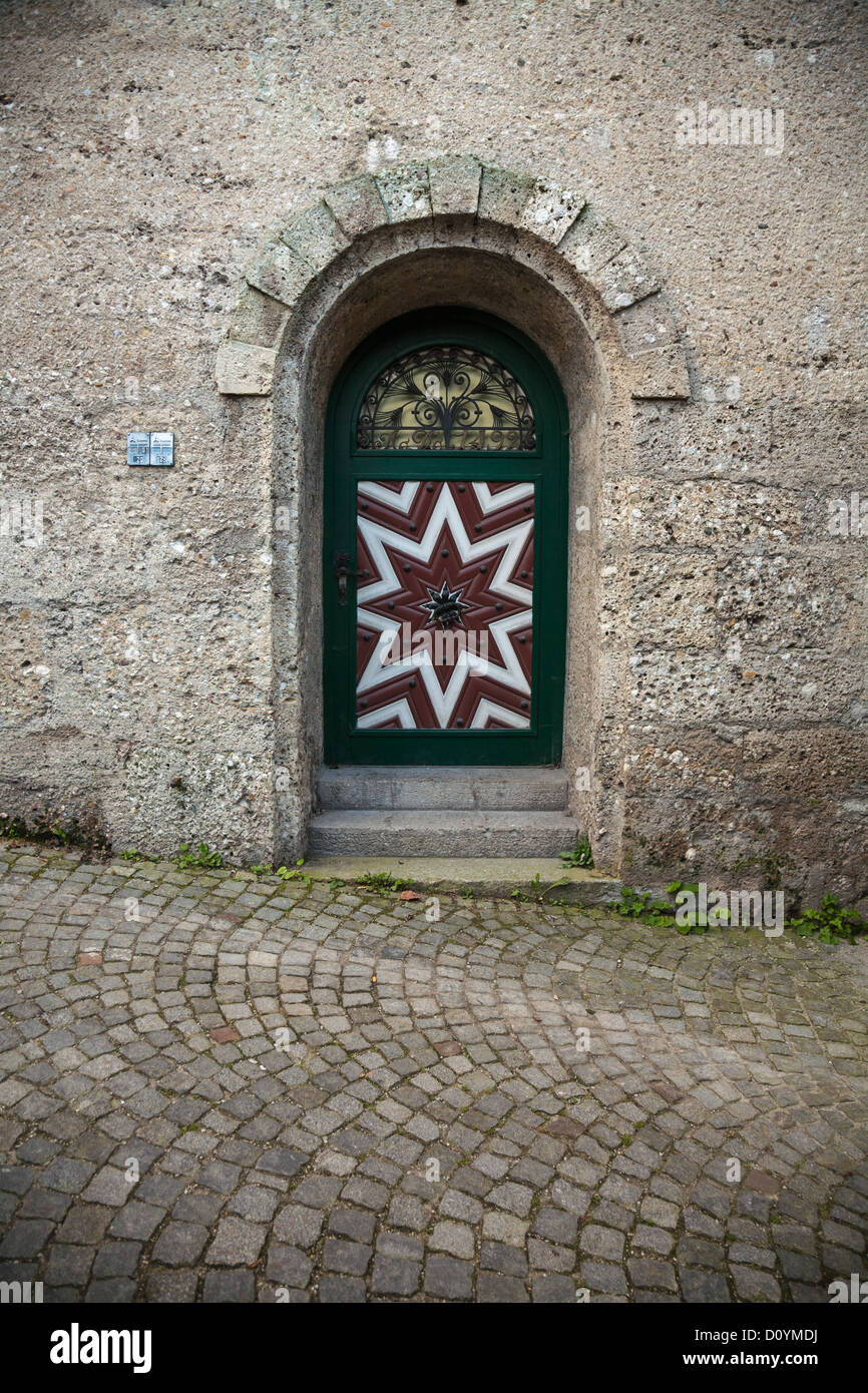 Dekorative und gewölbte rote und weiße Tür zur Salzburger Stieglkeller inmitten einer schweren Steinmauer mit Kopfsteinpflasterstraße. Stockfoto