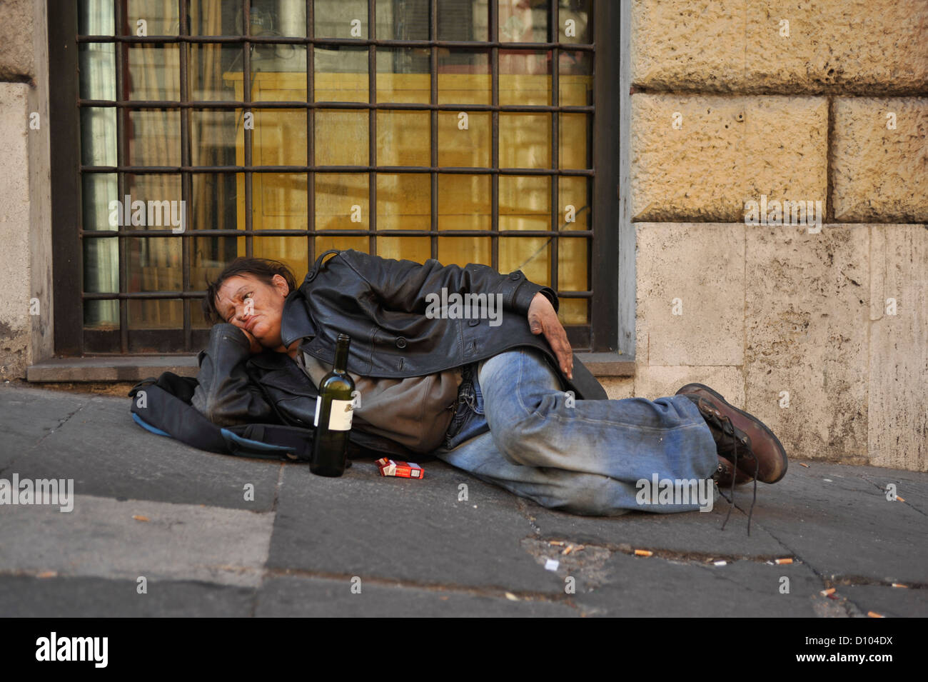 BETRUNKENE OBDACHLOSE FRAU VERZWEIFELT IN DEN STRAßEN VON ROM MIT EINER FLASCHE WEIN UND EINE PACKUNG ZIGARETTEN, Stockfoto