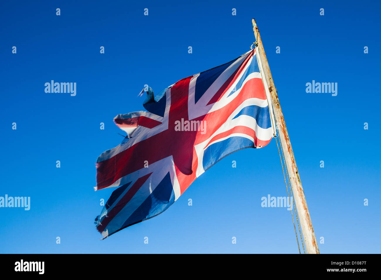 Zerlumpt, zerrissen und vernachlässigten Union Jack, die britische Nationalflagge, auf eine Fahnenstange vor einem strahlend blauen Himmel. Stockfoto