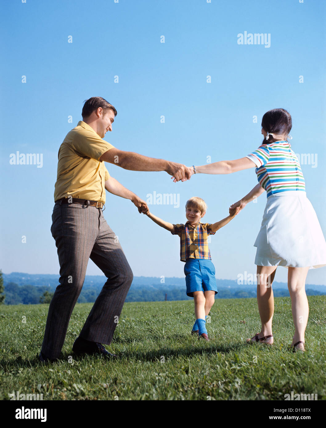 1970ER JAHRE FAMILIE MUTTER VATER BOY SPIELEN RING UM ROSEN, HAND IN HAND Stockfoto