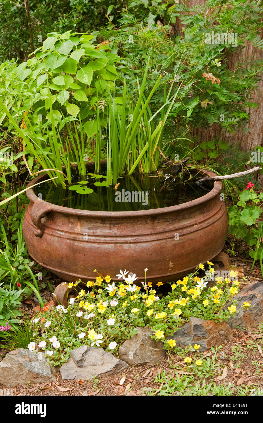 Reich verzierte Gartenteich - großen rostigen Kessel als ein Wasserspiel mit bunten Blumen und Wasserpflanzen Stockfoto