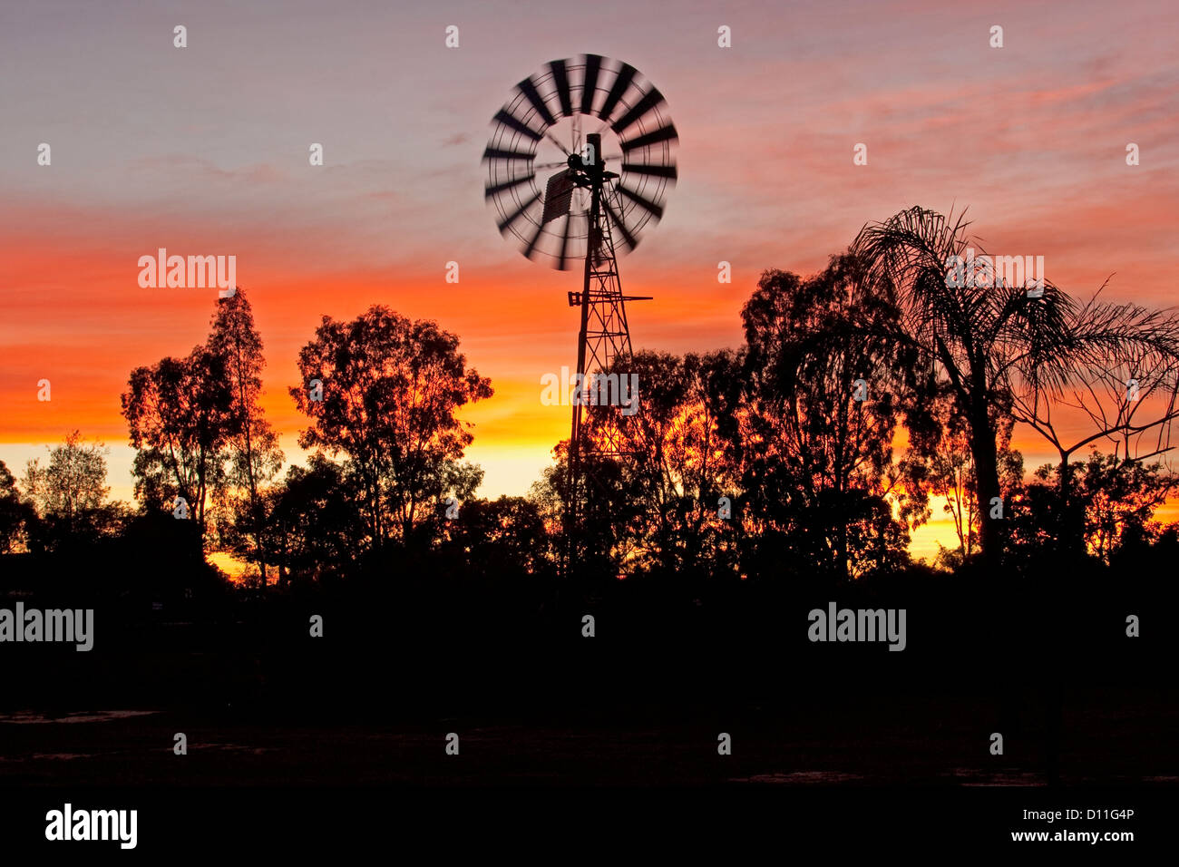 Windmühle bei Sonnenaufgang gegen bunte rot und gelb gestreift Himmel im australischen outback, im südwestlichen Queensland, Australien Stockfoto