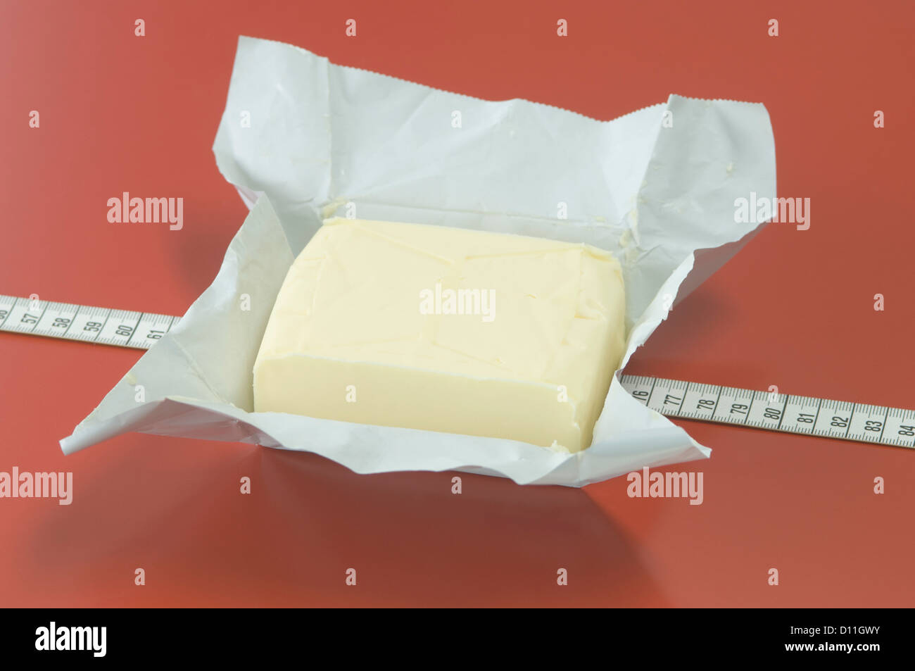 Block von Butter mit Maßband auf rotem Grund Stockfoto