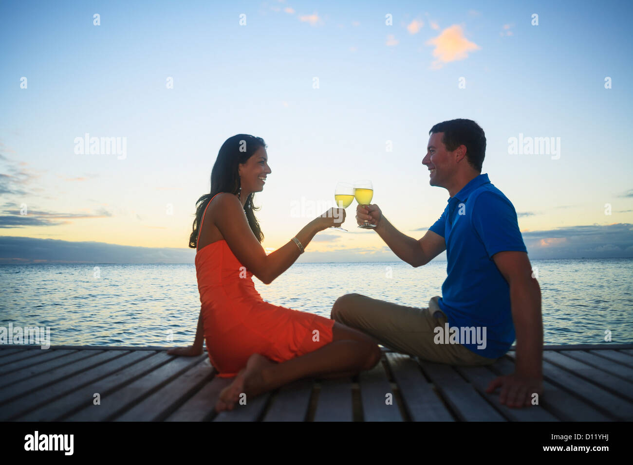 Mann und Frau bei einem Drink an der Wasserkante im Bora Bora Nui Resort And Spa Toasten; Gesellschaftsinseln, Südpazifik Stockfoto