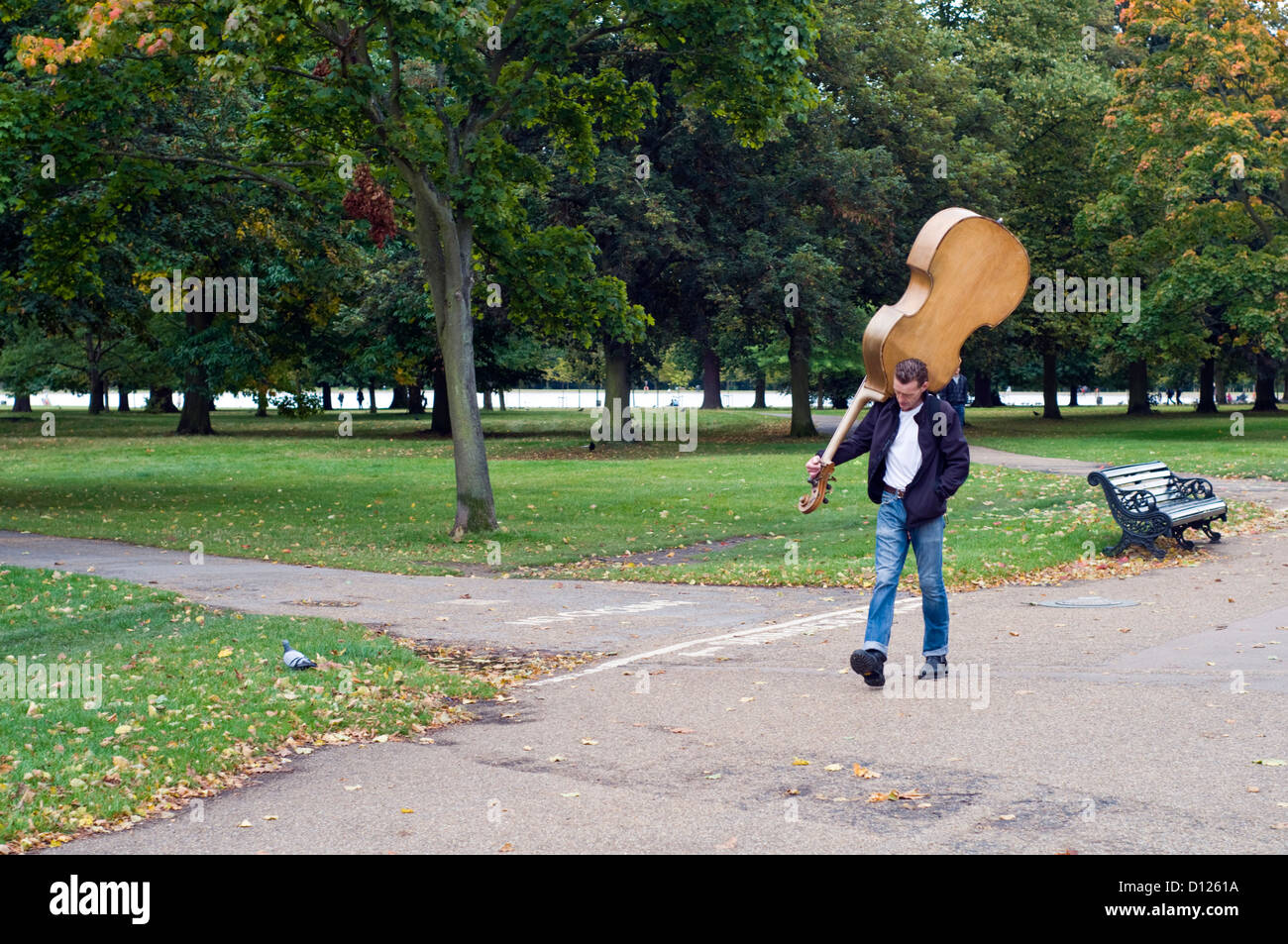 Ein Mann trägt einen Kontrabass durch den Hyde Park in London, England, UK Stockfoto