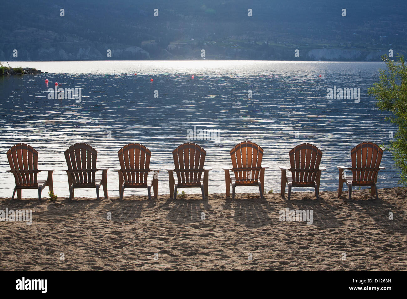 Aufgereiht an der Küste der Sonne reflektierenden See mit Schatten der Stühle auf dem Sand liegen; British Columbia Kanada Stockfoto