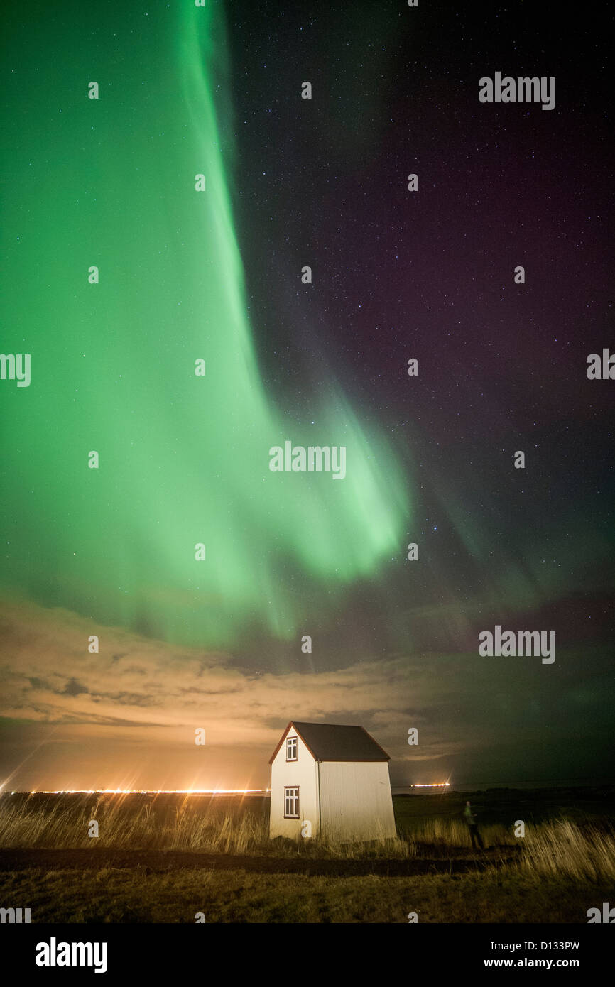 Grüne Streifen von Aurora Borealis Nordlichter über ein kleines Haus in einem Feld in Island Stockfoto
