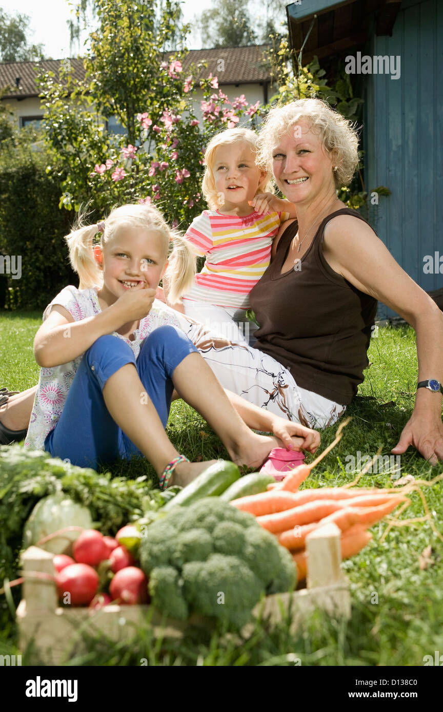 Deutschland, Bayern, Großmutter mit Kindern sitzen im Garten, Gemüse im Vordergrund Stockfoto