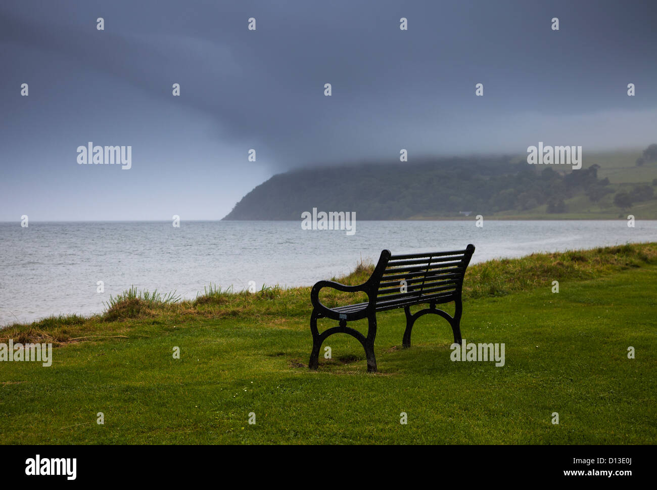 Eine Bank sitzt an der Wasserkante mit Gewitterwolken über dem Wasser; Moray Firth Schottland Stockfoto