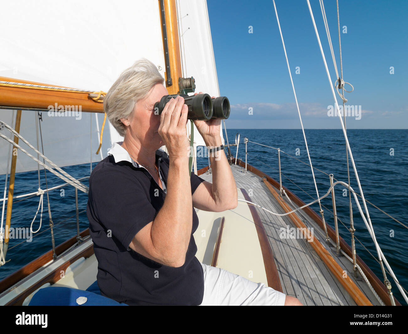 Ältere Frau mit dem Fernglas auf Segelboot Stockfoto