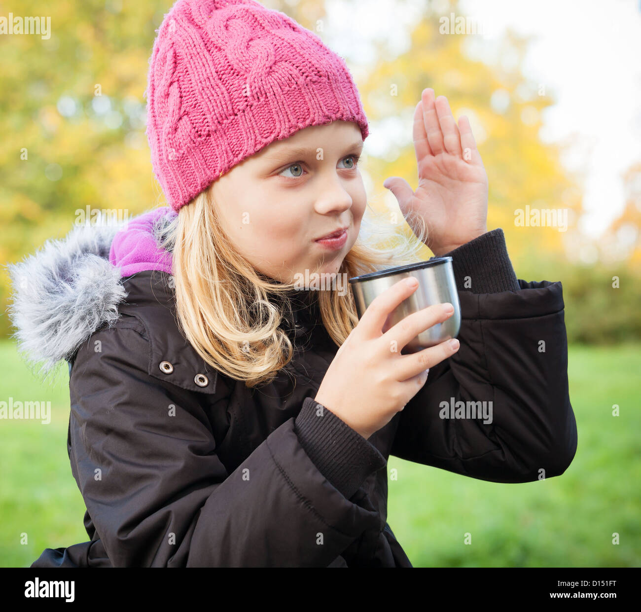 kleine schöne Blondine trinkt Tee im herbstlichen Park und die Hand hochzieht. Outdoor-Porträt. Stockfoto