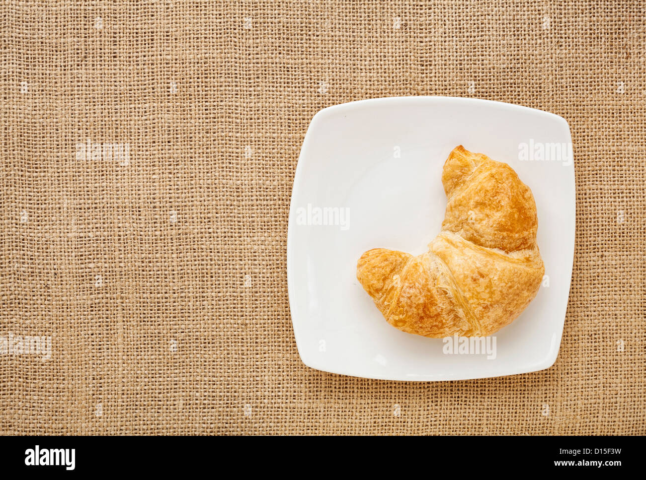 Croissant-Rolle auf einen weißen Porzellanteller gegen Sackleinen Leinwand Brett Stockfoto