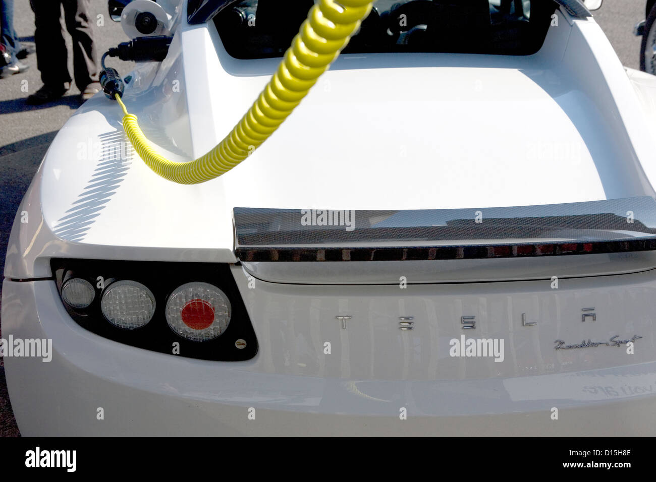 Ein Tesla Elektroauto mit seiner Batterie über eine gelbe Stromkabel aufgeladen. Stockfoto
