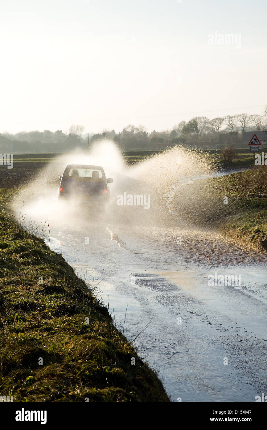Ein Auto durchläuft Flut mit Geschwindigkeit kotzte Spray auf einer Straße in North Norfolk, Großbritannien. Die Straßen wurde wegen starkem Regen Herbst & das Regenwasser läuft aus der Felder auf den Highway überflutet. Stockfoto