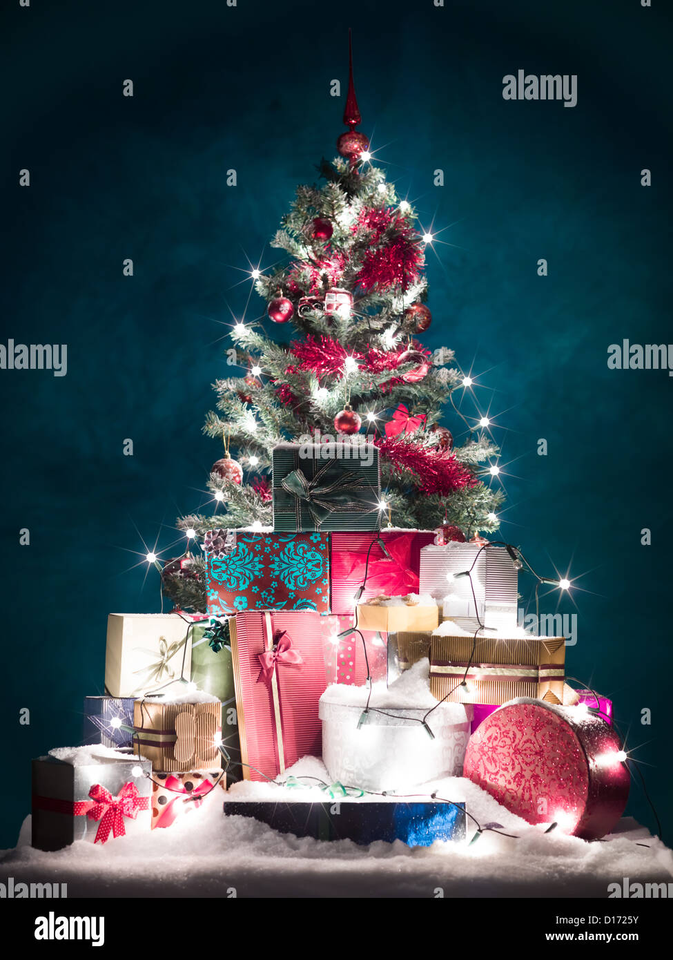 geschmückter Weihnachtsbaum mit roten Verzierungen und glänzend weiße  Lichter, umgeben von bunten Geschenke mit Schnee bedeckt, vor blauem  Hintergrund mit Farbverlauf Licht Stockfotografie - Alamy