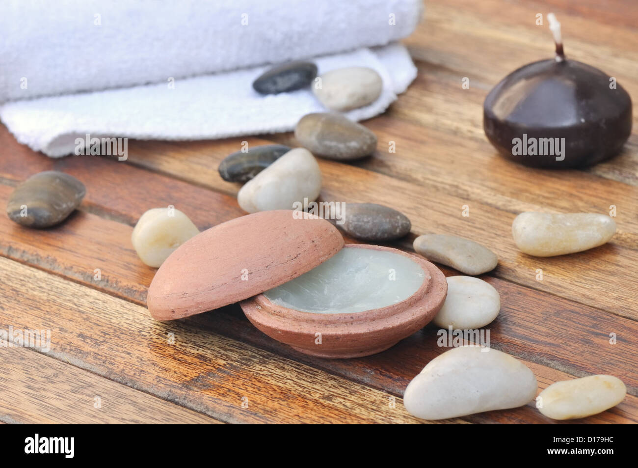 Massage-Balsam in einem kleinen Tontopf mit Steinen und ein Handtuch auf die hölzernen Latten gelegt Stockfoto