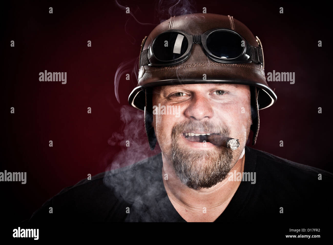 Biker in einem Helm raucht eine Zigarre auf dunklem Hintergrund Stockfoto