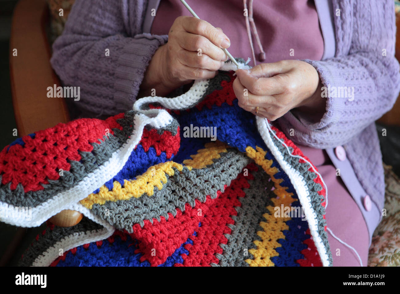 Ältere Frau Häkeln bunte Decke für wohltätige Zwecke zu Hause, Suffolk, UK Stockfoto