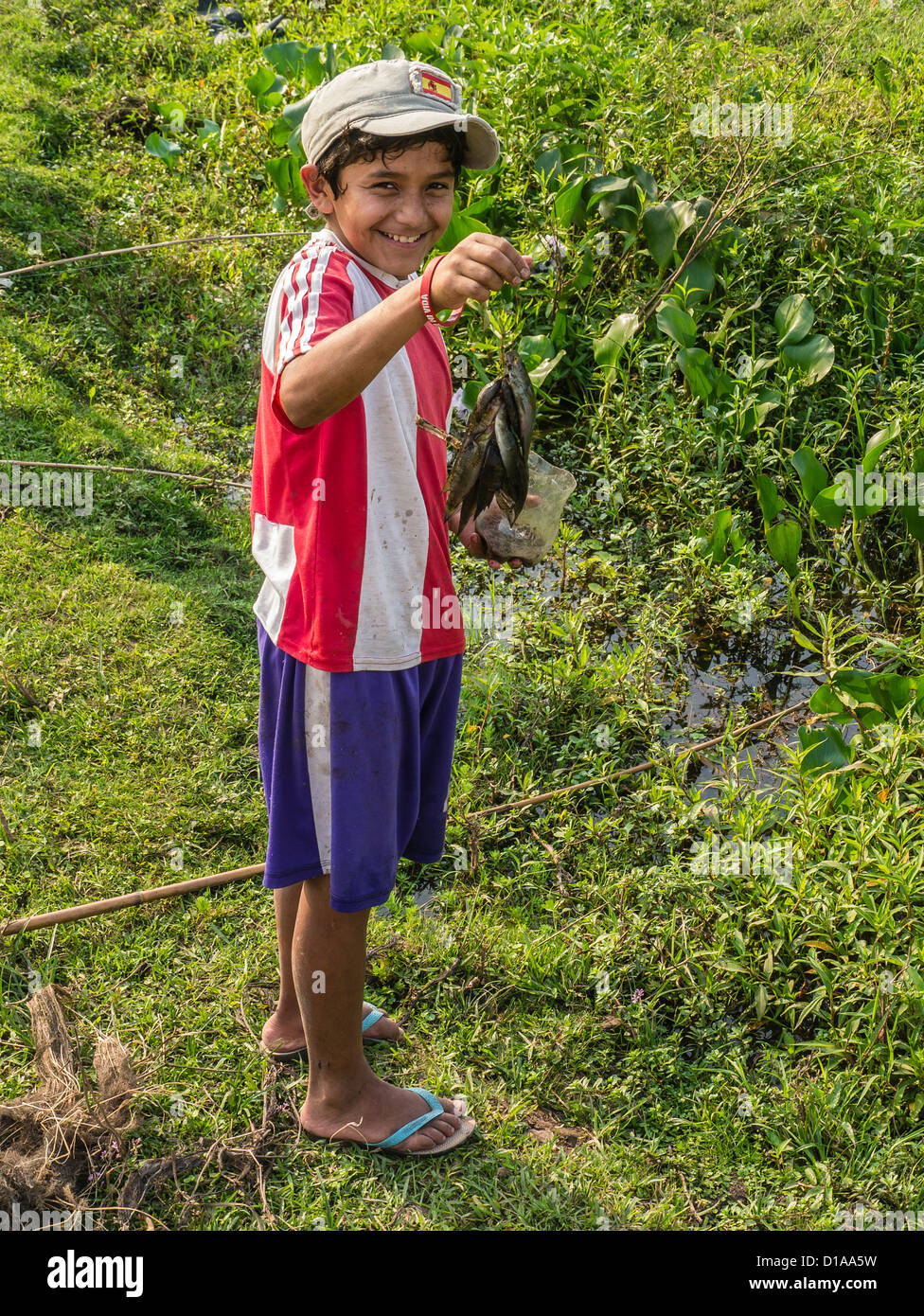 Ein Junge paraguayischen lächelt wie er blickt nach vorne hält seine frisch gefangenen Fisch aus einem Bach in der Nähe seiner Heimat. Stockfoto