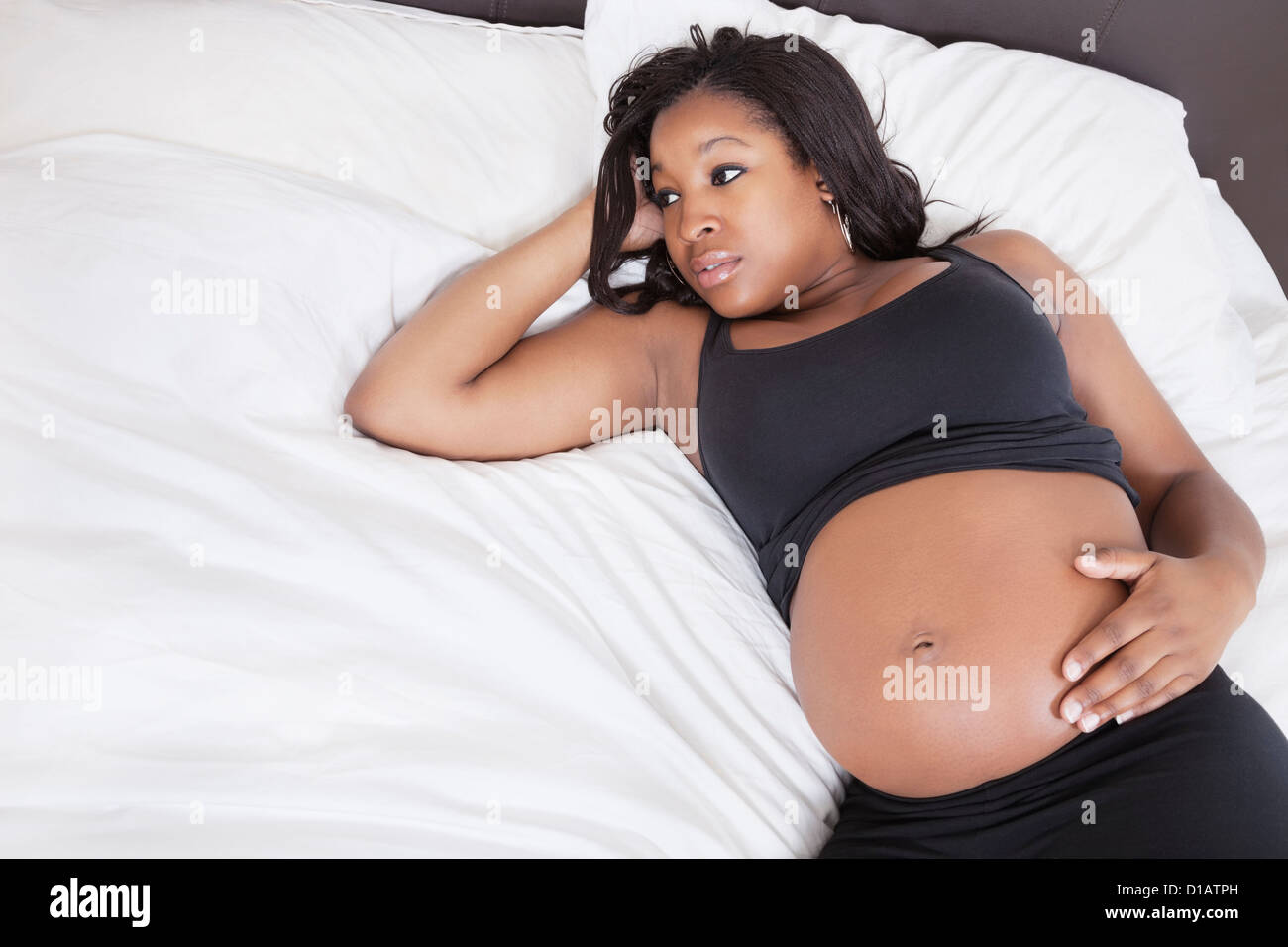 Nachdenkliche junge schwangere Frau im Bett liegend Stockfoto