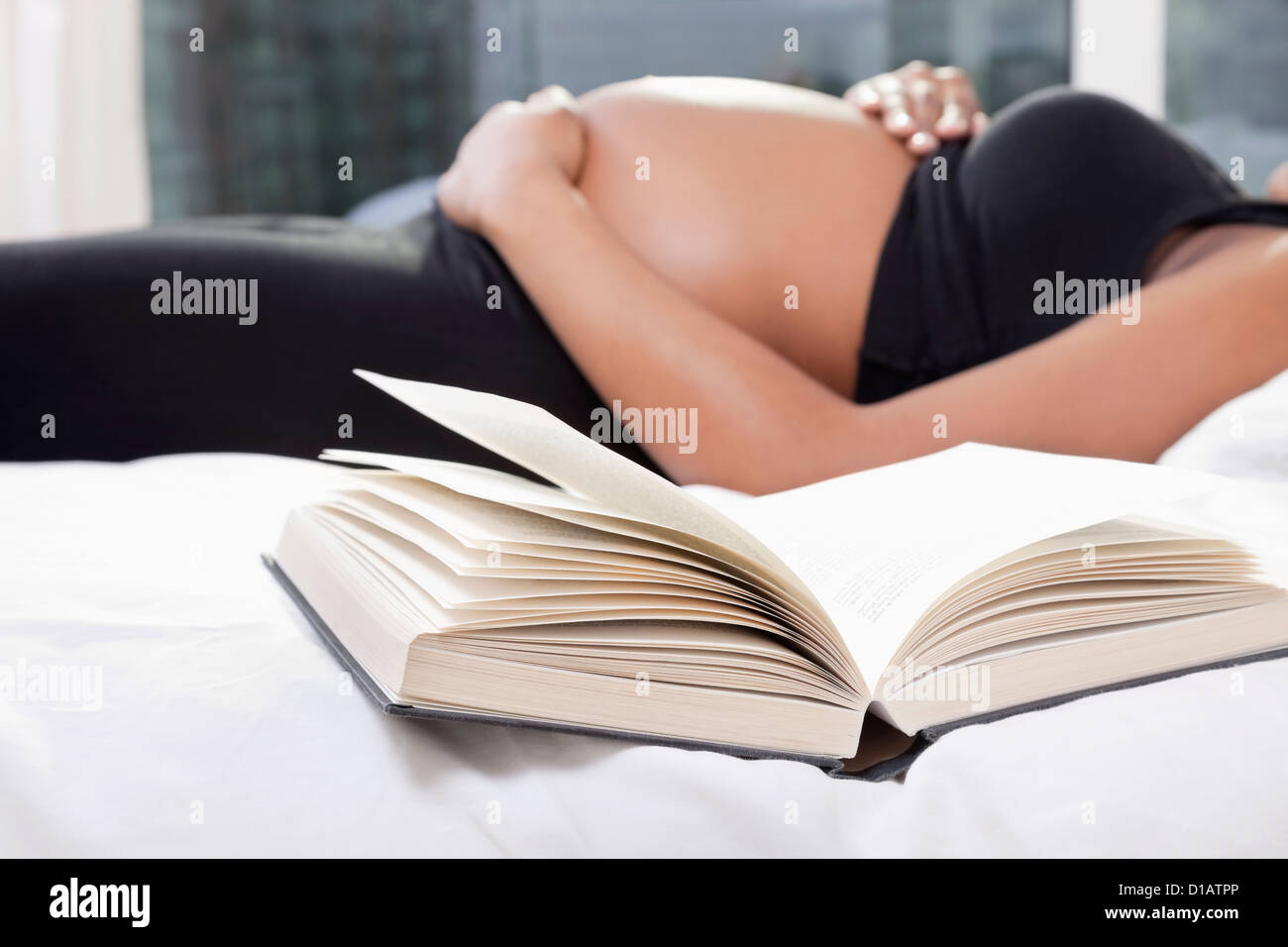 Öffnen Sie Buch Mitte Abschnitt schwangere Frau im Bett liegend im Vordergrund Stockfoto