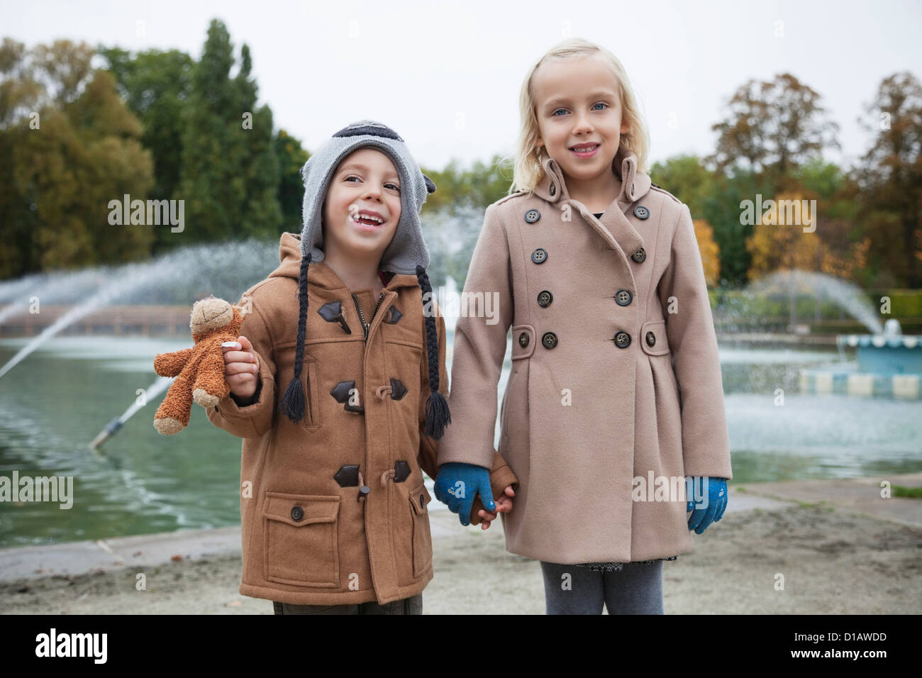 Porträt glücklich Bruder Schwester in Trenchcoats, die Hand in Hand im park Stockfoto